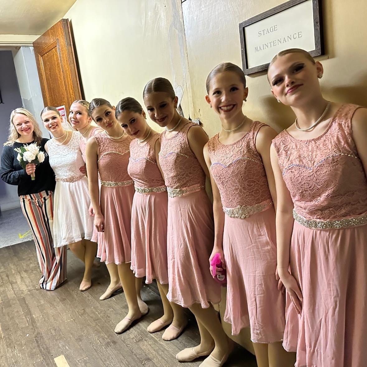 Dancers in pink costumes posing with their instructor backstage