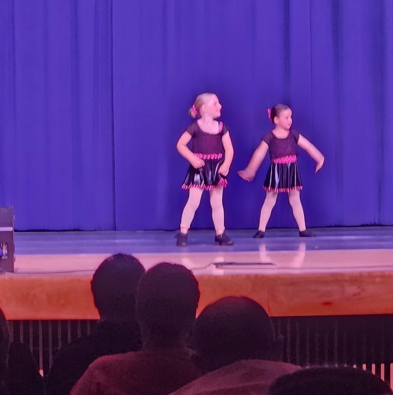 Two young dancers performing together under purple stage lighting