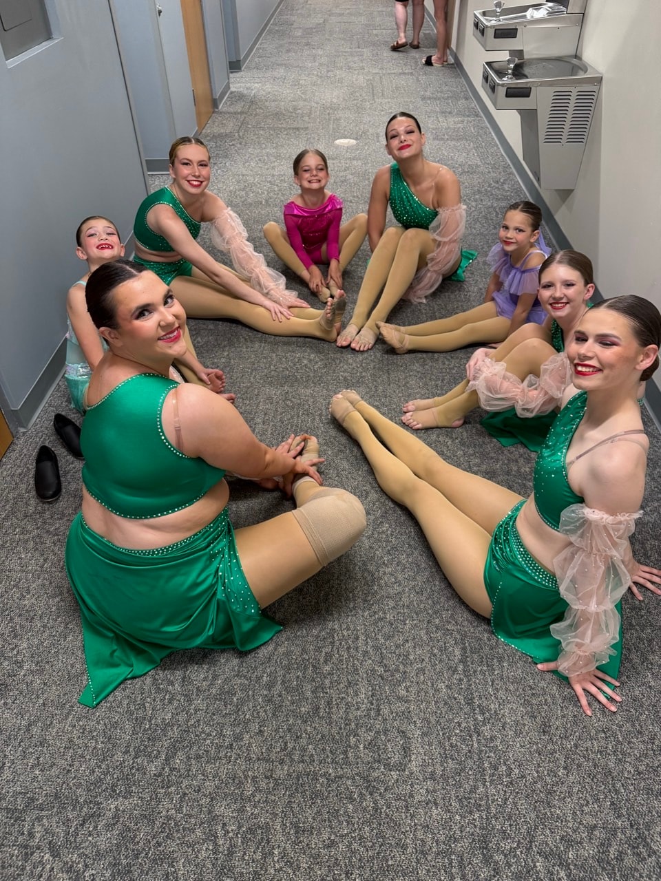 Turn Out Dance Academy dancers relaxing together backstage in green and purple costumes