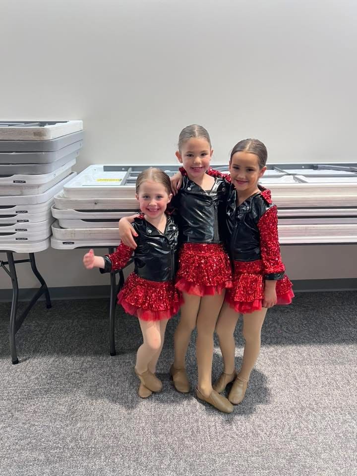 Three young dancers posing backstage in red and black costumes