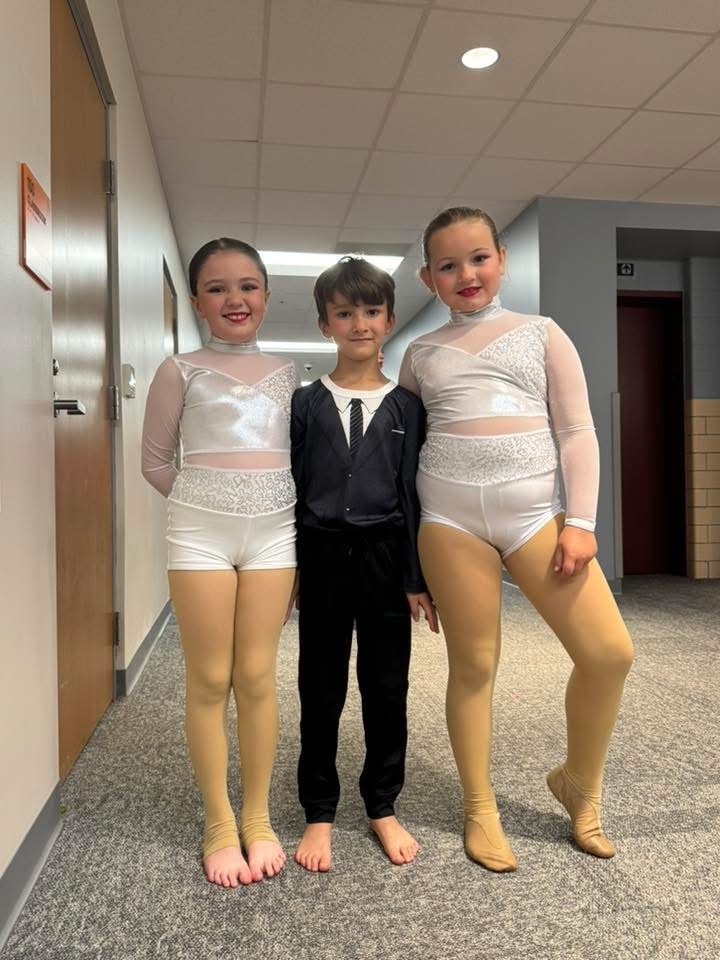 Three young dancers posing backstage in white performance costumes