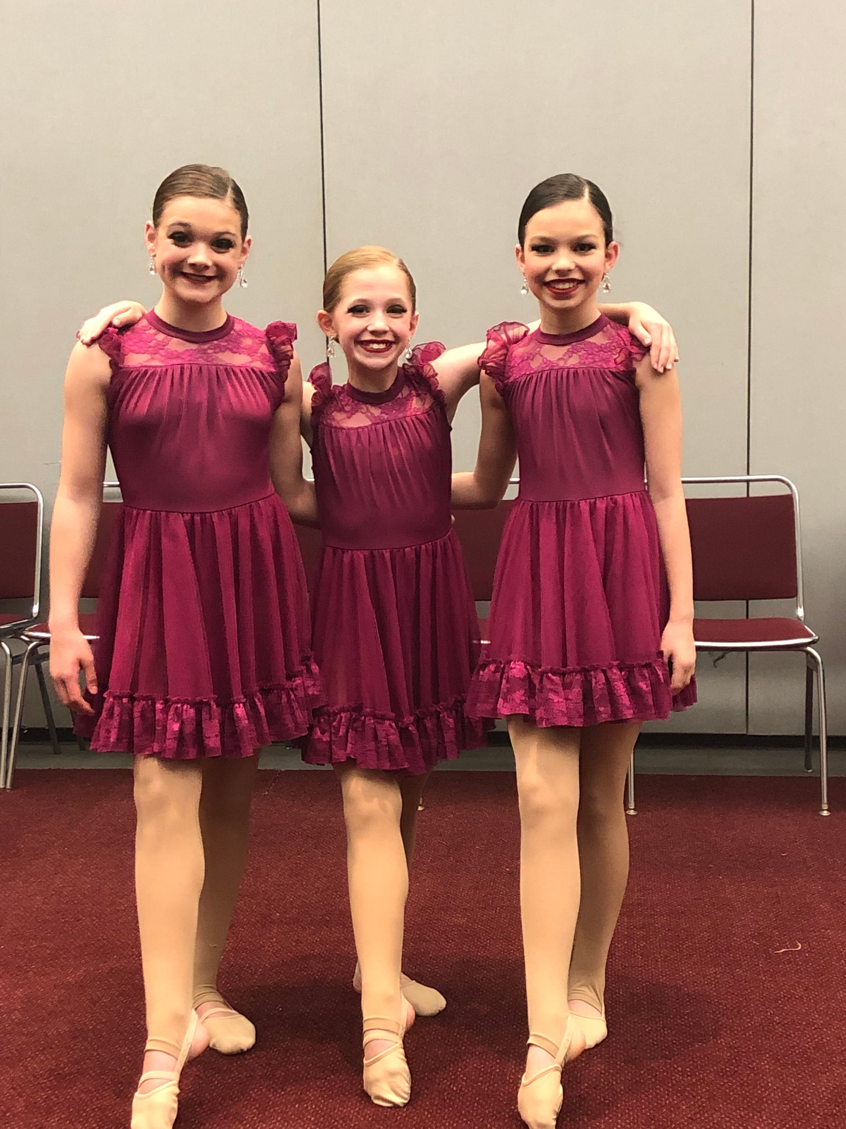 Three dancers posing together in matching burgundy recital costumes