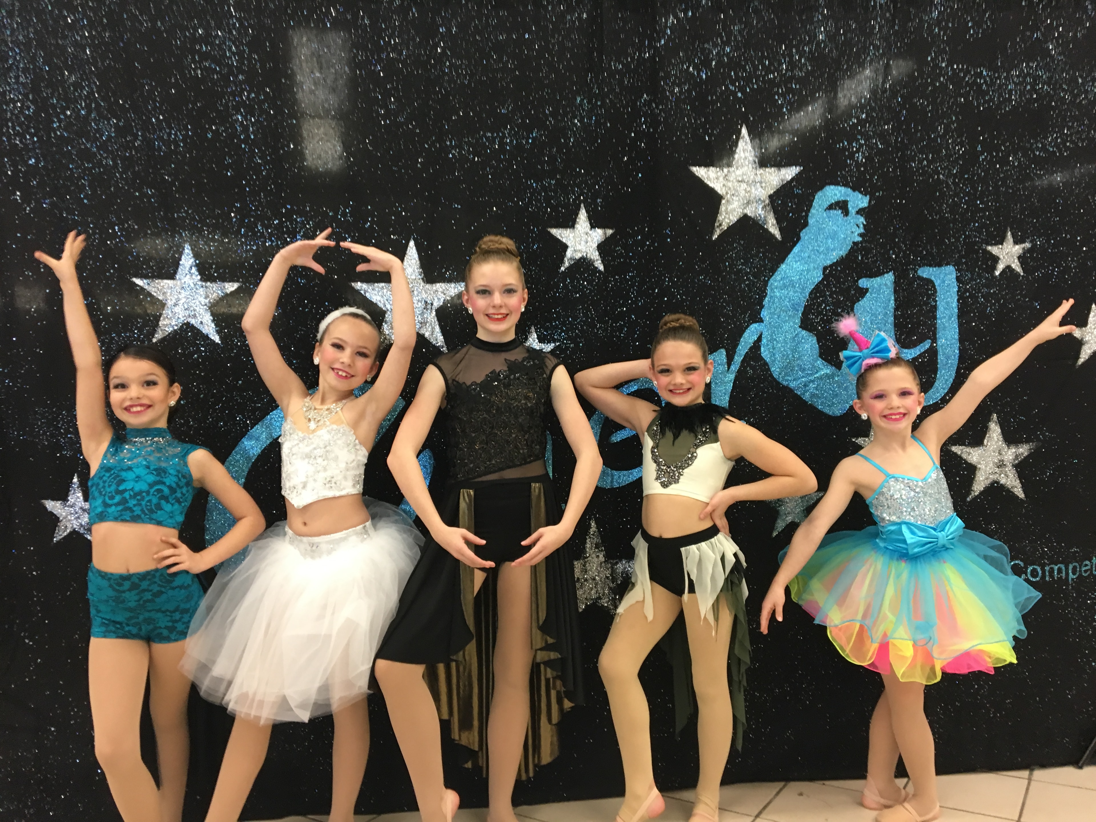 Young dancers posing in colorful recital costumes before a starry performance backdrop