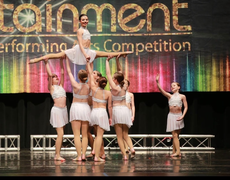 Dance team performing a lift in white costumes on a competition stage