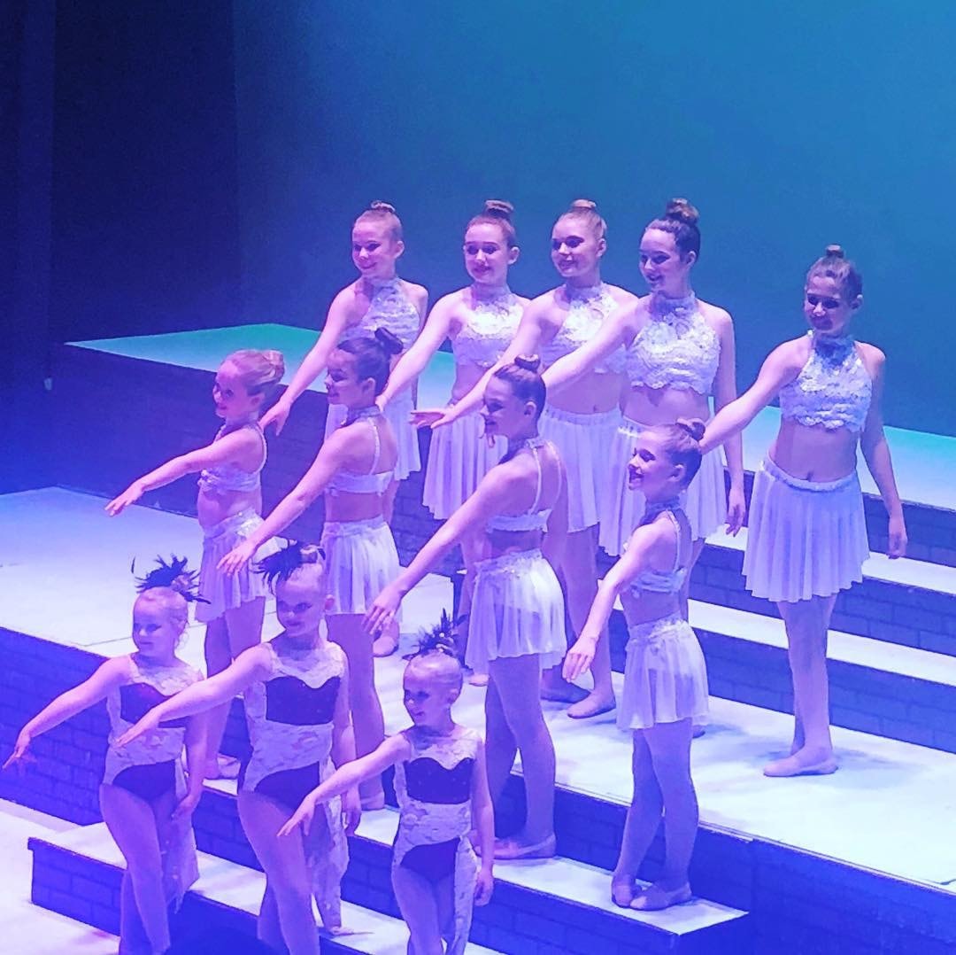 Young dancers performing in white costumes on illuminated recital stage steps