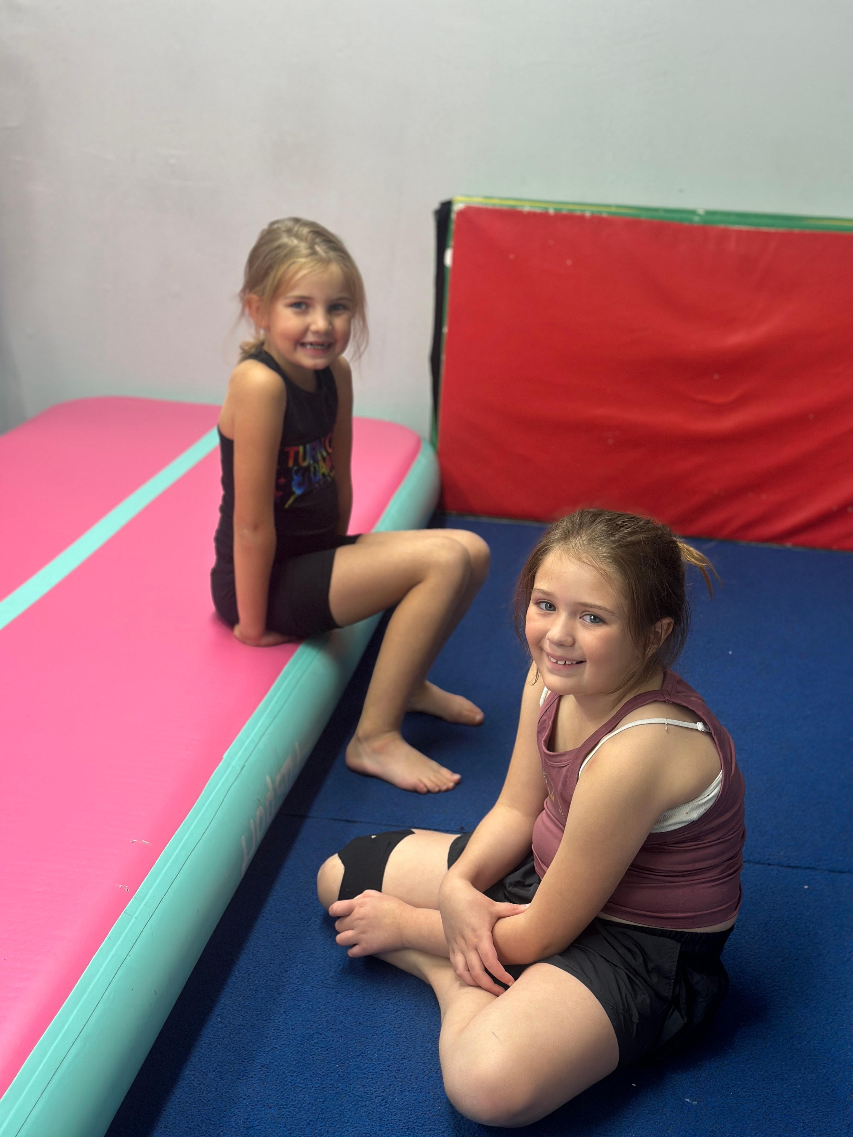 Two young dancers smiling together on gymnastics mats